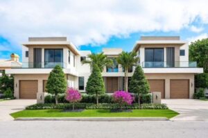 A symmetrical pair of modern two-story homes with large glass balconies, attached garages, and landscaped front yards.
