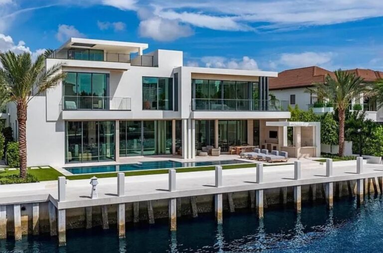 A modern multi-story waterfront house with large glass windows, a swimming pool, and a dock.