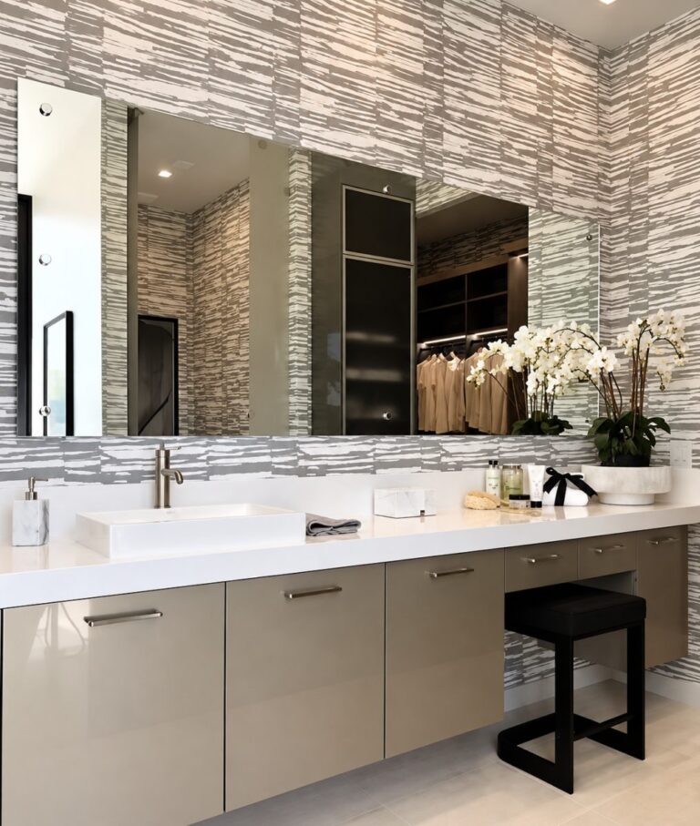 A modern bathroom vanity with a large wall mirror, rectangular vessel sink, beige cabinets, patterned wallpaper, and potted white orchids on the countertop.