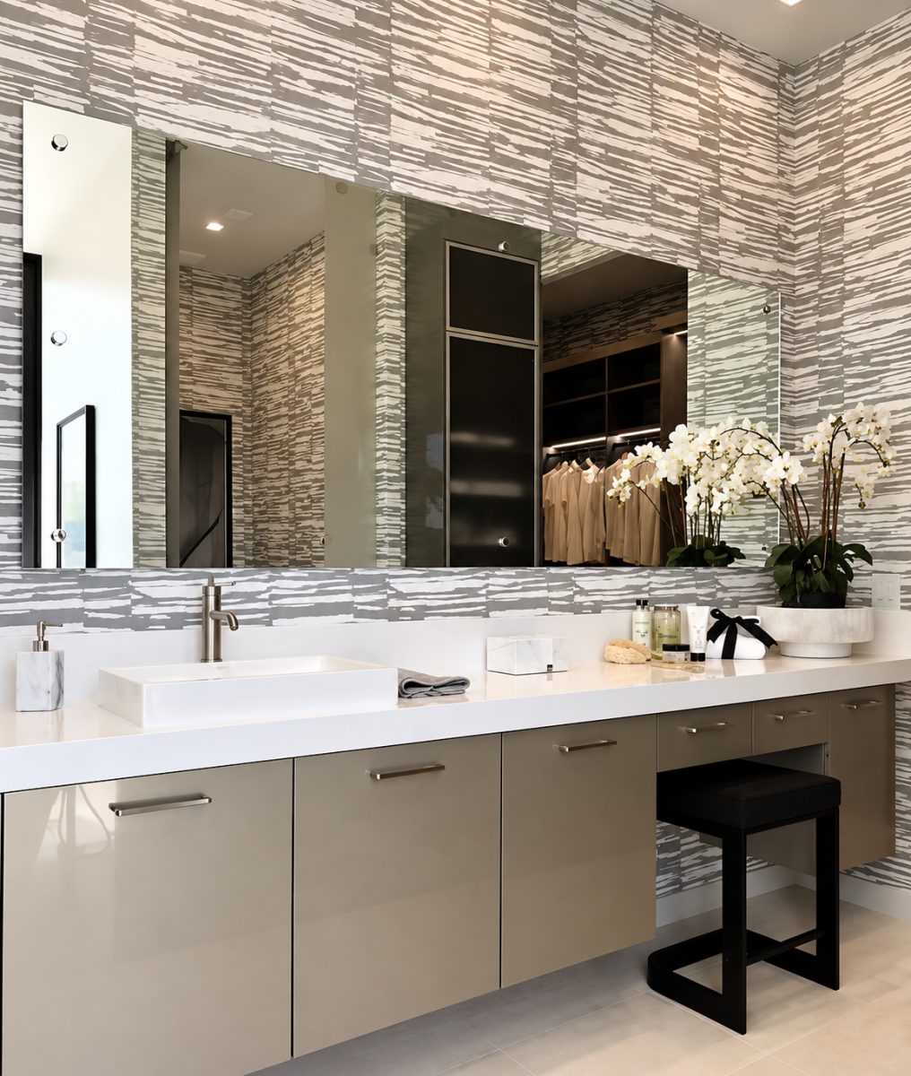 A modern bathroom vanity with a large wall mirror, rectangular vessel sink, beige cabinets, patterned wallpaper, and potted white orchids on the countertop.