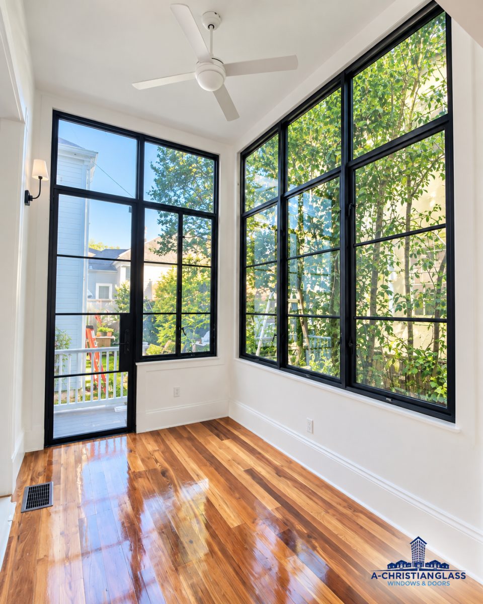 A bright interior room features large black-framed windows and a glass door looking out to trees.