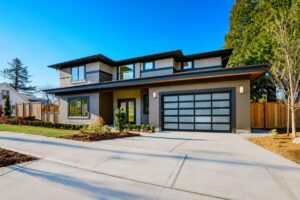 A modern two-story house with a glass-panel garage door and landscaped front yard is shown under a clear blue sky.